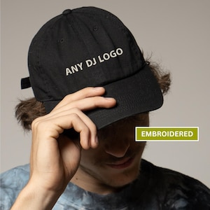 May include: Black baseball cap with the text "ANY DJ LOGO" embroidered in white. The cap has a curved brim and an adjustable strap. The word "EMBROIDERED" is in a green rectangle.