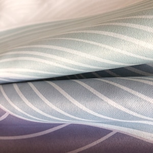 May include: Close-up of a fabric with a wavy, striped pattern in shades of blue and white. The fabric is folded over, revealing a purple and white striped pattern underneath.