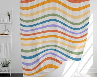 Puede incluir: Una cortina de ducha con un patrón de rayas onduladas en tonos de naranja, amarillo, verde, azul y morado. La cortina está colgada en un baño con una bañera blanca.