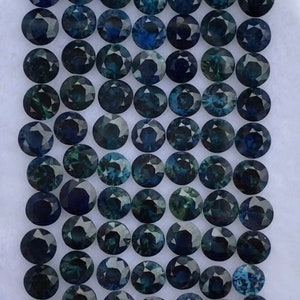 May include: A collection of 72 round, faceted, dark blue gemstones. The gemstones are arranged in a grid pattern on a white surface.