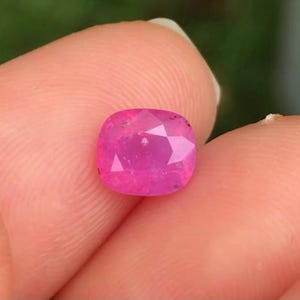 May include: A pink gemstone with a cushion cut. The gemstone is set in a ring.
