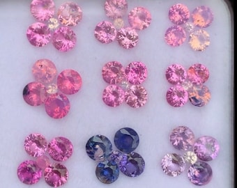 May include: Nine flower-shaped arrangements of gemstones in shades of pink, purple, and blue. Each arrangement consists of five to seven round-cut stones. The gemstones are displayed in a white tray with a black border.