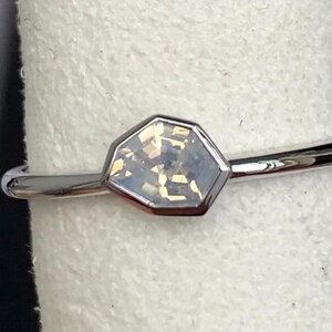 Puede incluir: Un anillo de plata con una piedra preciosa iridiscente hexagonal. La piedra est&aacute; engastada en un bisel de plata y tiene un aspecto claro y multicolor. La banda es fina y pulida.