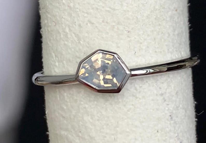 Puede incluir: Un anillo de plata con una piedra preciosa iridiscente hexagonal. La piedra est&aacute; engastada en un bisel de plata y tiene un aspecto claro y multicolor. La banda es fina y pulida.