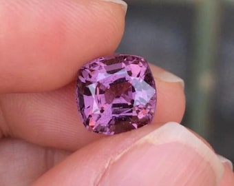 May include: A cushion-cut pink sapphire gemstone with a purplish hue.