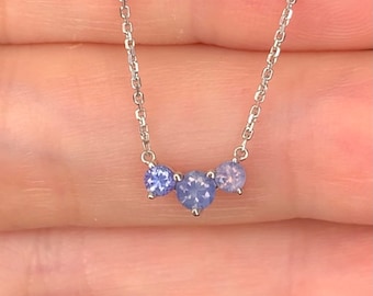 Puede incluir: Un collar de cadena de plata con tres pequeñas piedras azules. Las piedras preciosas son redondas y tienen un ligero brillo.