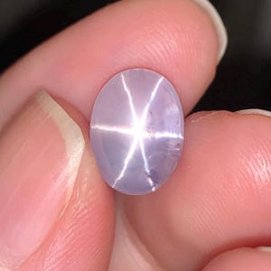 May include: A light purple star sapphire gemstone with a star-shaped reflection in the center.