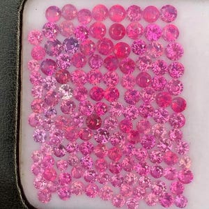 May include: A collection of pink sapphires in a variety of shades and sizes, displayed in a white tray with a black border.