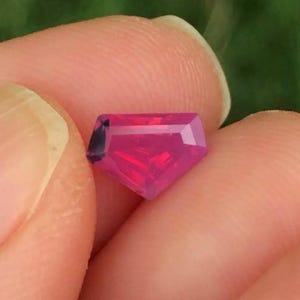 May include: A vibrant pink gemstone with a faceted cut. The gemstone is a deep pink colour and has a slightly irregular shape.