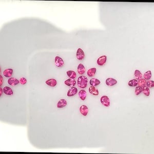 May include: A collection of pink pear-shaped gemstones arranged in three flower shapes.