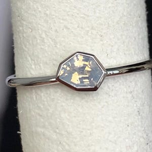 Puede incluir: Un anillo de plata con una piedra preciosa hexagonal e iridiscente. La piedra preciosa est&aacute; engastada en un bisel y tiene un aspecto claro y multicolor. La banda es fina y pulida.