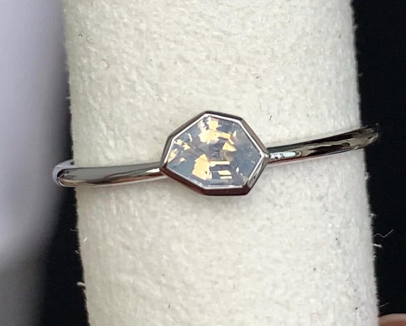 Puede incluir: Un anillo de plata con una piedra preciosa hexagonal e iridiscente. La piedra preciosa est&aacute; engastada en un bisel y tiene un aspecto claro y multicolor. La banda es fina y pulida.