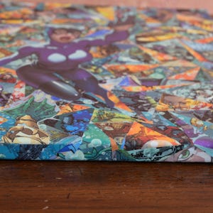 May include: A close-up of a canvas painting with a collage of colorful comic book pages. The painting features a woman in a purple costume, with a blue and green background.