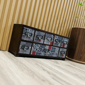 May include: A wooden box with nine small drawers. The drawers are lined with a patchwork fabric featuring red, blue, and white patterns.