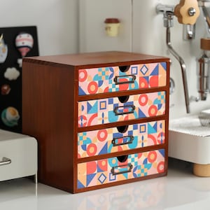 May include: A small, wooden storage chest with four drawers. The drawers are decorated with a colorful geometric pattern in shades of red, blue, and orange. Each drawer has a small, metal pull.