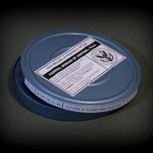 May include: A blue metal film canister with a white label reading THIS RECORD IS PROPERTY OF THE FEDERAL BUREAU OF CONTROL, U.S.A. and a side label reading BRIGHT FALLS, WA OLD GODS OF ASGARD BAND REHEARSAL. The canister has a circular lid.