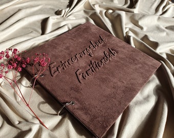 Op de afbeelding: Een bruin suède fotoalbum met zilveren ringen. De omslag is gegraveerd met de tekst "Erinnerungsbuch Familienclub".