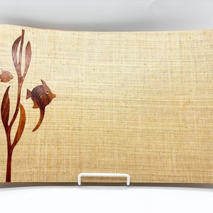 May include: Rectangular serving tray with a woven, beige surface. The tray features a decorative design of two fish and seaweed cut from dark brown wood. A white metal stand supports the tray.