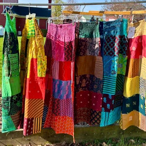 May include: A selection of patchwork skirts in various colours hanging on a clothesline. The skirts display a range of patterns and hues, including red, pink, green, yellow, and blue. The skirts are made from different fabrics and have a bohemian style.