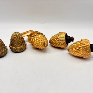 May include: Five gold-colored metal pine cone shaped bottle stoppers. The stoppers have a detailed design and are perfect for adding a touch of elegance to any wine collection.