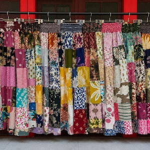 May include: A collection of long skirts hanging on a rack, each featuring a patchwork design composed of various fabric squares. The skirts display a wide array of floral, geometric, and abstract patterns in diverse colours including pink, blue, yellow, and green, all finished with a gathered elastic waistband.