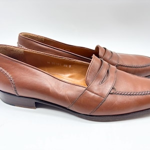 May include: A pair of brown leather penny loafers. The shoes have a classic design with a rounded toe, a strap across the vamp, and a low heel. The stitching is visible around the edges. The shoes are size 9.5 D.