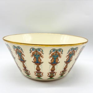 May include: Cream-colored ceramic bowl with a gold rim and ornate, repeating pattern in teal, orange, and brown. The bowl's design features stylized floral and scroll motifs, creating a vintage aesthetic. A decorative piece for serving or display.