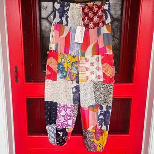 Könnte beinhalten: Patchworkhose mit einer Vielzahl farbenfroher Stoffmuster, darunter Blumen-, Paisley- und geometrische Designs. Die Hose hängt an einer roten Tür. Sie hat einen elastischen Bund und eine lockere, bequeme Passform.