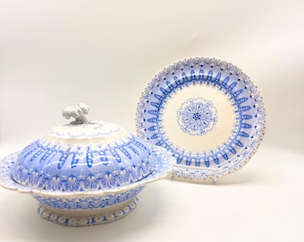 Op de afbeelding: Een witte en blauwe porseleinen serveerschaal met een deksel en een bijpassend bord. De schaal heeft een gegolfde rand en een bloemenmotief. Het bord heeft een vergelijkbaar ontwerp.