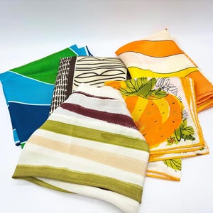 May include: A collection of colorful vintage silk scarves. The scarves feature various patterns, including stripes, geometric designs, and fruit illustrations. Colors include green, blue, orange, yellow, and brown. The scarves are folded and arranged on a white surface.