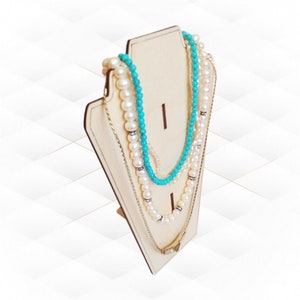 May include: A cream-coloured wooden jewellery display stand holding several necklaces. The necklaces feature white pearls, turquoise beads, and silver chains. Some necklaces have rhinestone details. The stand is angled.