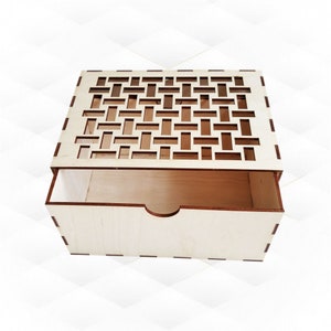 May include: A light-colored wooden box with a decorative, openwork top. The box has a rectangular shape with a drawer that is partially pulled out, revealing the interior. The top features a geometric pattern, and the box appears to be made of unfinished wood.