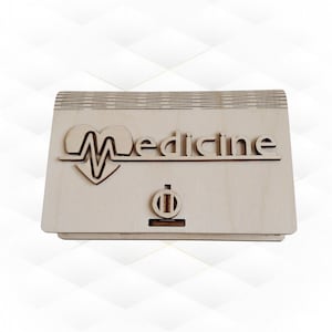 以下が含まれることがあります： 前面にハートと「Medicine」という文字が刻まれた木製の箱。箱の前面には小さな丸い穴が開いています。