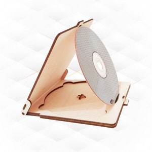 May include: A wooden CD or DVD case with a hinged lid and a slot for a disc. The case is open and a silver disc is visible inside.