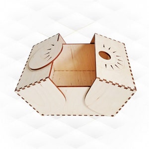 Puede incluir: Una caja de madera hexagonal con una tapa con bisagras. La caja está hecha de madera de color claro y tiene un diseño decorativo en la tapa.