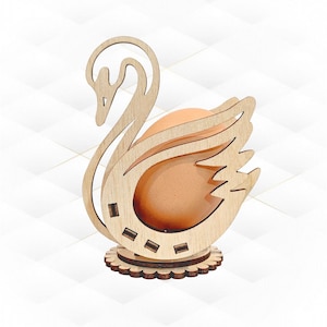 Pode incluir: Porta-ovos de madeira em forma de cisne com um ovo castanho no seu interior. O cisne é esculpido com detalhes intrincados e tem uma base com uma borda festoneada.