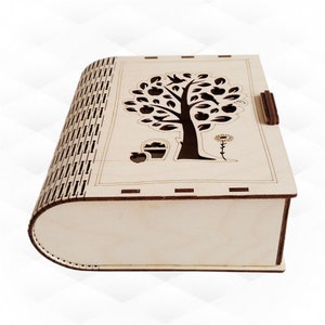 Puede incluir: Una caja de madera con un diseño recortado de un árbol con manzanas y pájaros. La caja tiene una tapa con bisagras y un acabado de madera natural.