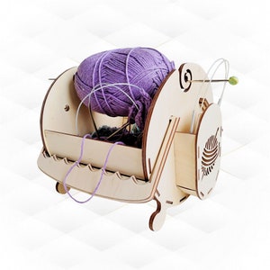 Puede incluir: Cuenco de madera para hilo con una bola de hilo morado y agujas de tejer. El cuenco tiene una guía de hilo incorporada y un compartimento de almacenamiento para las agujas de tejer.