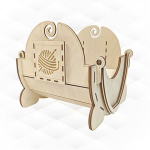 Pode incluir: Uma tigela de fio de madeira com um design decorativo. A tigela apresenta um painel quadrado com uma bola de fio e um gancho esculpidos. As laterais têm uma forma curva com redemoinhos decorativos no topo. A tigela é feita de madeira clara.