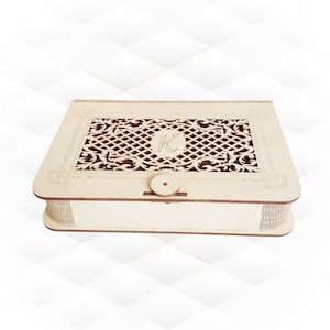 Puede incluir: Una caja de madera con un diseño decorativo cortado con láser en la tapa. El diseño presenta un patrón geométrico con una letra "K" en el centro. La caja tiene una tapa con bisagras y un pequeño cierre de botón.