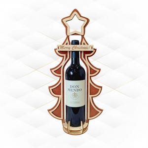 以下が含まれることがあります： 木製のクリスマスツリー型ワインボトルホルダー。上部に星が付いています。ホルダーは明るい茶色と濃い茶色の木材でできており、「Merry Christmas!」の文字がバナーに書かれています。ドンメンドワインのボトルが中に入っています。