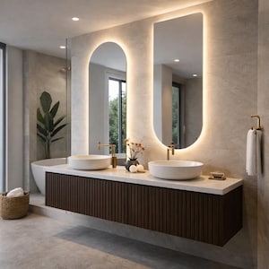May include: Modern bathroom design featuring two illuminated mirrors, a floating vanity with a dark wood finish, and two white vessel sinks. The space includes gold fixtures, a bathtub, and a decorative plant, creating a spa-like atmosphere.