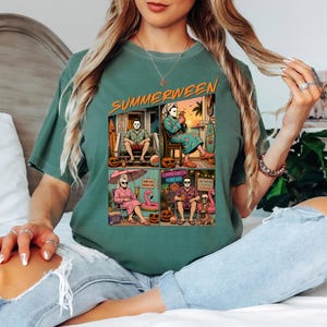 May include: A sage green t-shirt featuring a graphic print with the text SUMMERWEEN. The design consists of four panels showing a masked character in various summer vacation settings, including a beach house, a patio, and poolside with pumpkins.