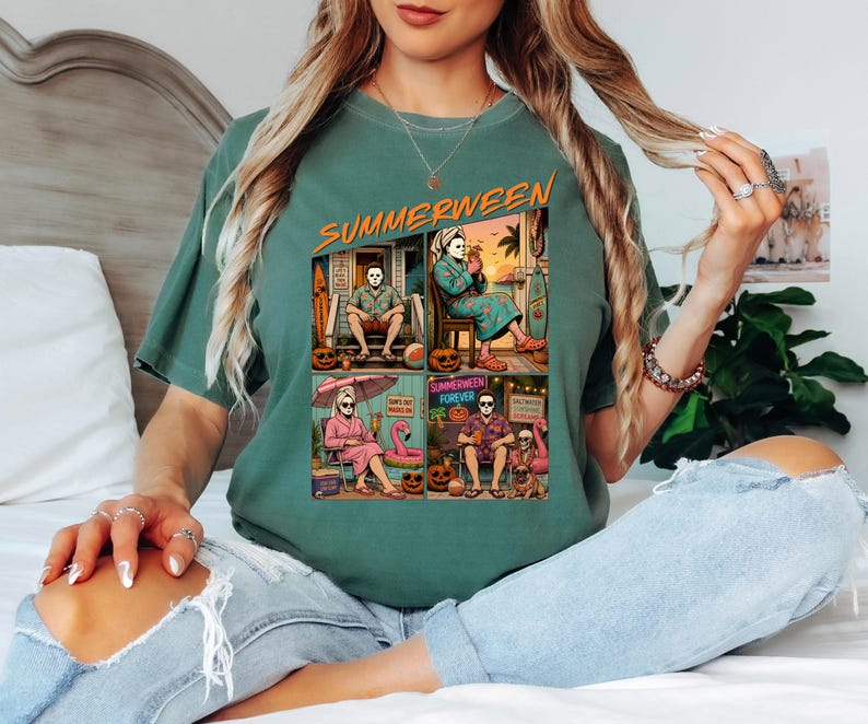 May include: A sage green t-shirt featuring a graphic print with the text SUMMERWEEN. The design consists of four panels showing a masked character in various summer vacation settings, including a beach house, a patio, and poolside with pumpkins.