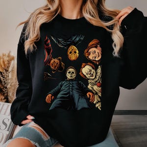 May include: Black sweatshirt featuring a colorful graphic of horror movie characters, including Freddy Krueger, Jason Voorhees, Michael Myers, Chucky, and Pennywise. The design is a collage of iconic villains, perfect for fans of the horror genre.