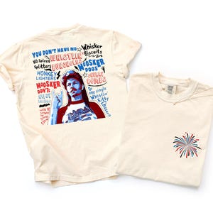 May include: Two cream-colored t-shirts. One features a graphic of a man with text that reads "YOU DON'T HAVE NO WHISTLIN' BUNCHOLES" and other phrases. The other shirt has a small firework design on the pocket area.