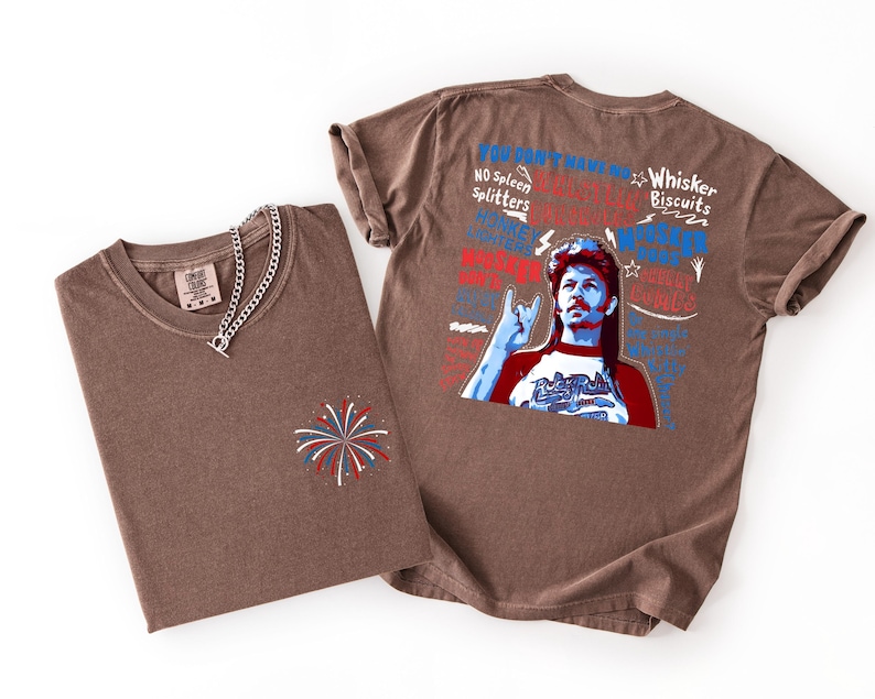May include: Two brown t-shirts with a graphic print. One shirt is folded with a silver chain necklace and a firework design. The other shirt has a graphic of a man with text that reads "You Don't Have No Spleen Splitters" and "Whisker Biscuits".
