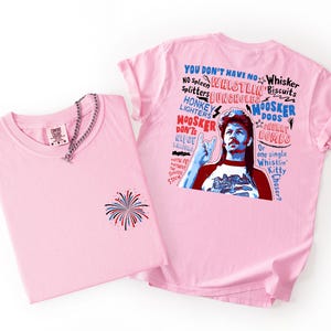 May include: Two pink t-shirts. One has a firework design on the front and a silver chain. The other has a graphic of a man with text that reads "YOU DON'T HAVE NO WHISTLIN' BISCUITS".