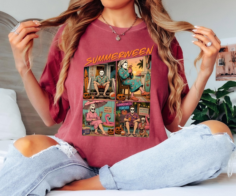 May include: A maroon t-shirt featuring a graphic print with the text "SUMMERWEEN" at the top. The graphic is divided into four panels showing a masked character in various summer settings, including a porch, a patio, a beach chair, and a lounge.