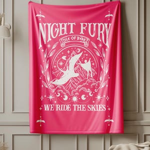 May include: A vibrant pink throw blanket with the words "NIGHT FURY" in white, along with an illustration of a dragon and the text "WE RIDE THE SKIES." The design is framed by decorative elements.
